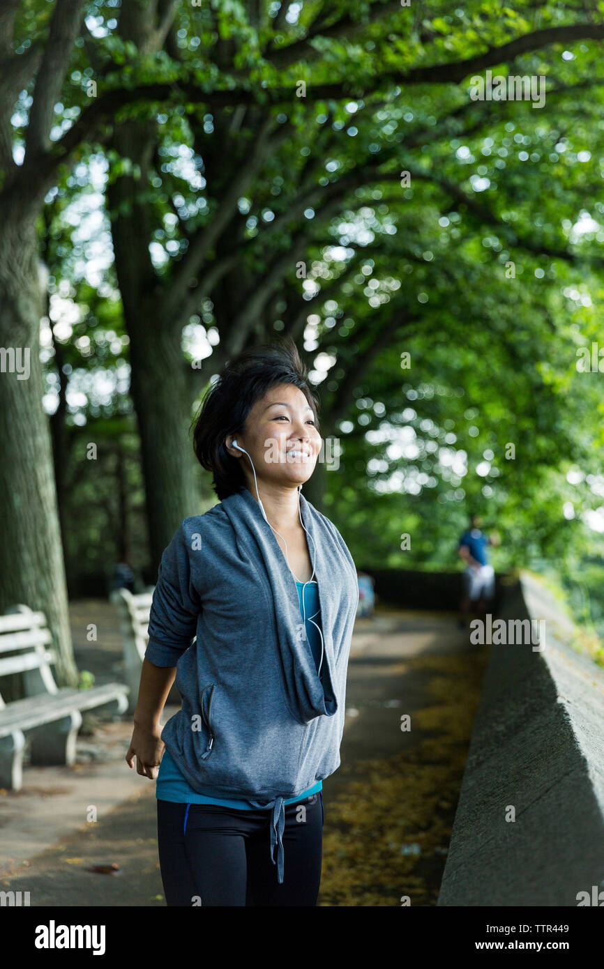 Frau stretching Arme hinter dem Rücken, während der Wiedergabe von Musik auf Fußweg gegen Bäume Stockfoto
