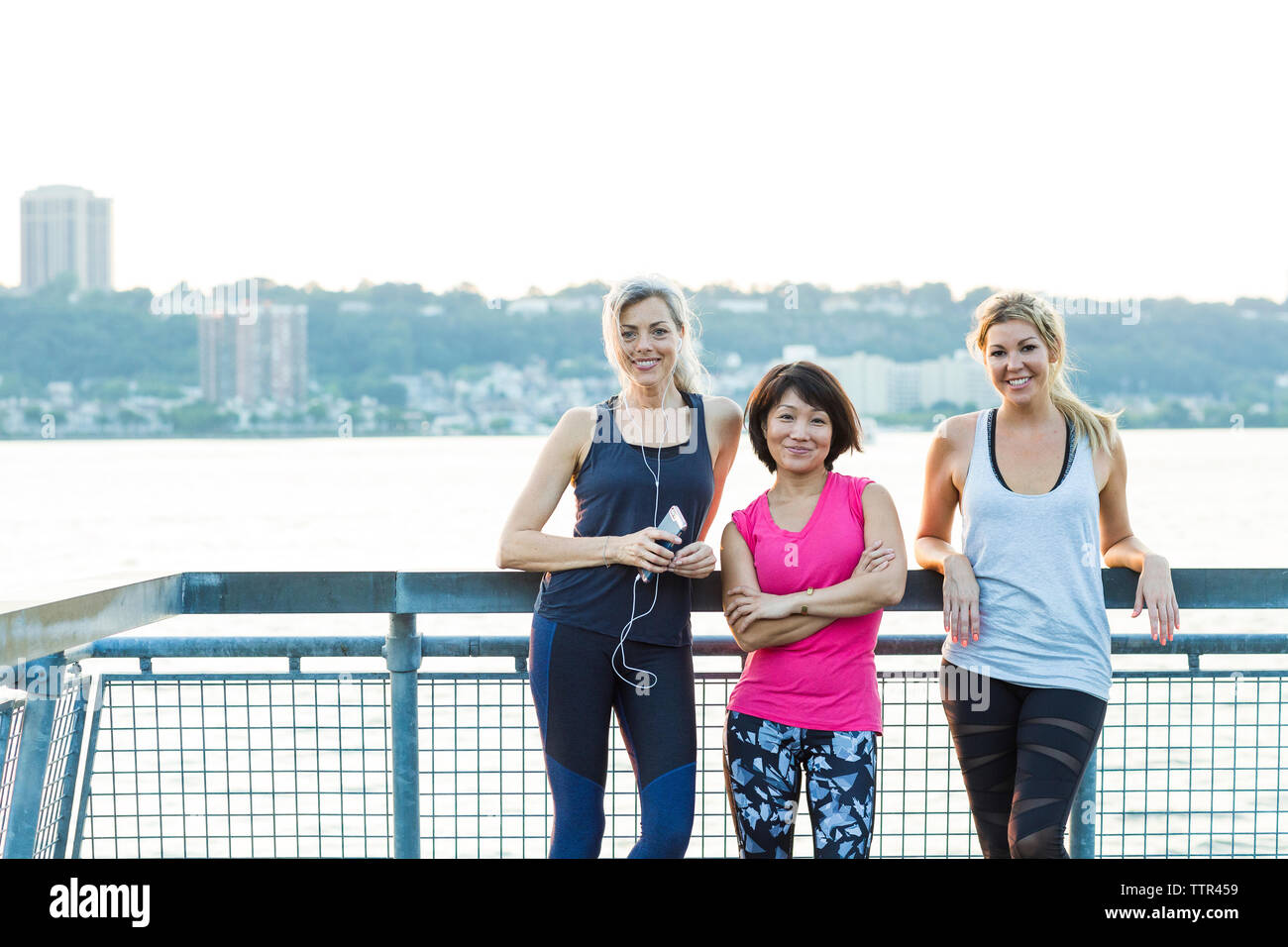 Portrait von zuversichtlich weibliche Freunde im Sport Kleidung beim Stehen auf der Brücke gegen den klaren Himmel Stockfoto