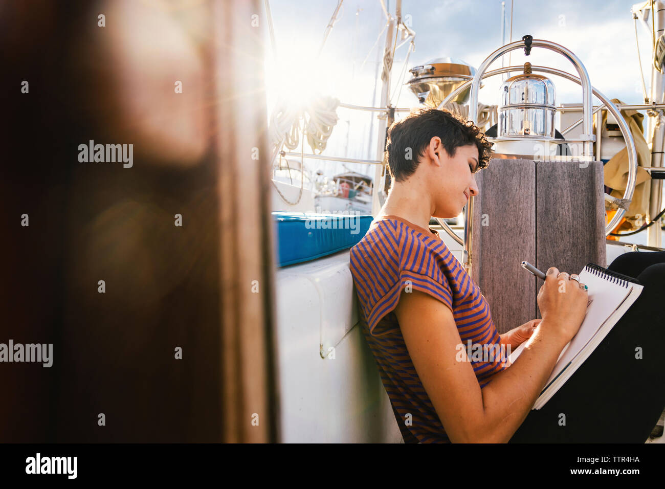 Seitenansicht der Frau schriftlich beim Sitzen auf Buchen Sie im Boot durch das Fenster gesehen Stockfoto