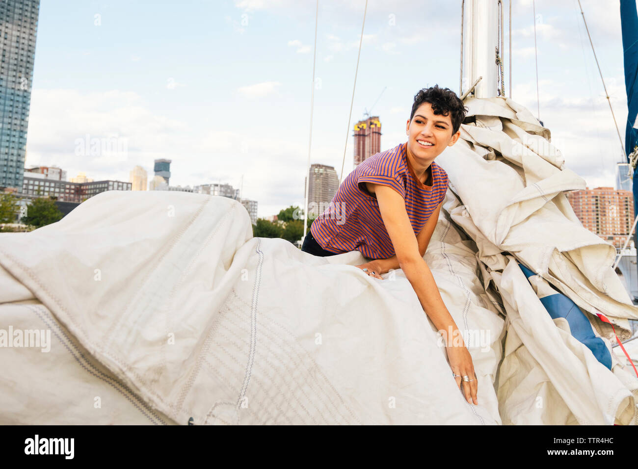 Lächelnde Frau mit Segel beim Stehen in der Boot gegen Sky Stockfoto