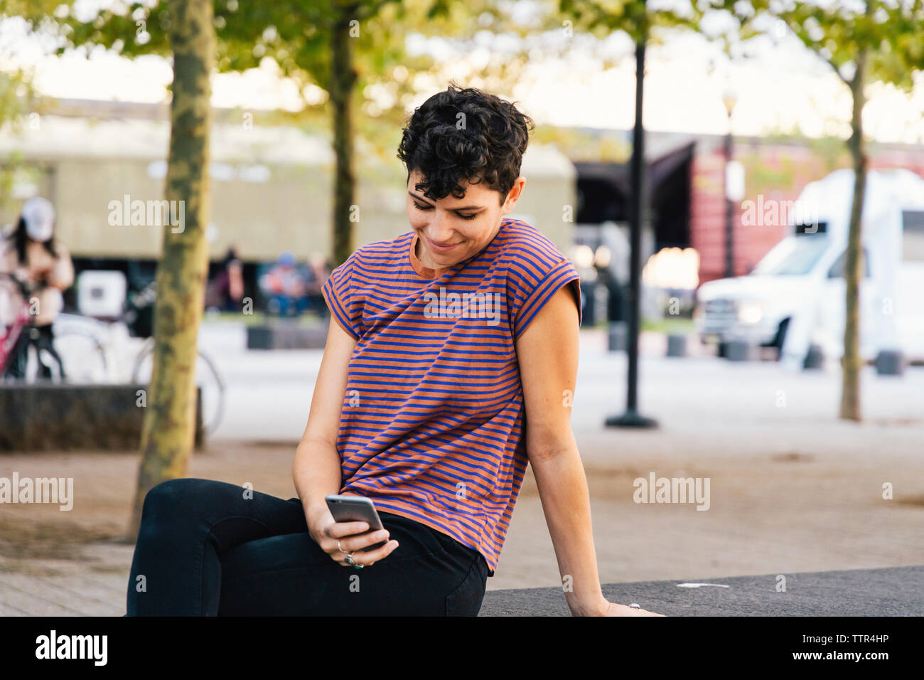 Lächelnde Frau mit Smart Phone während im Park sitzen Stockfoto