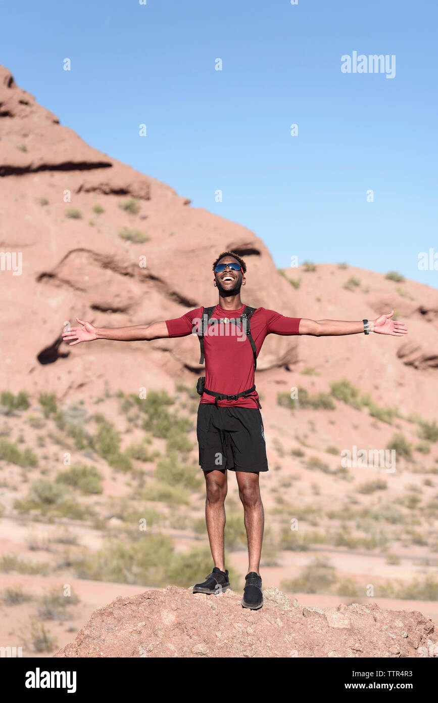 Männliche Wanderer mit ausgestreckten Armen auf Rock gegen blauen Himmel während der sonnigen Tag Stockfoto