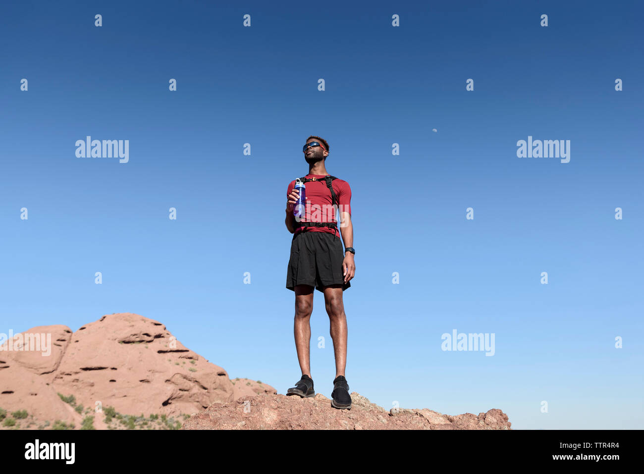 Low Angle View männlicher Wanderer holding Wasserflasche beim Stehen auf Rock Formation gegen den klaren blauen Himmel Stockfoto