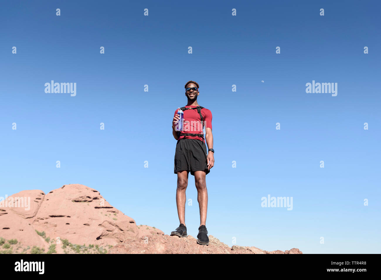 Low Angle View männlicher Wanderer mit Wasserflasche stehen auf Rock Formation gegen den klaren blauen Himmel Stockfoto