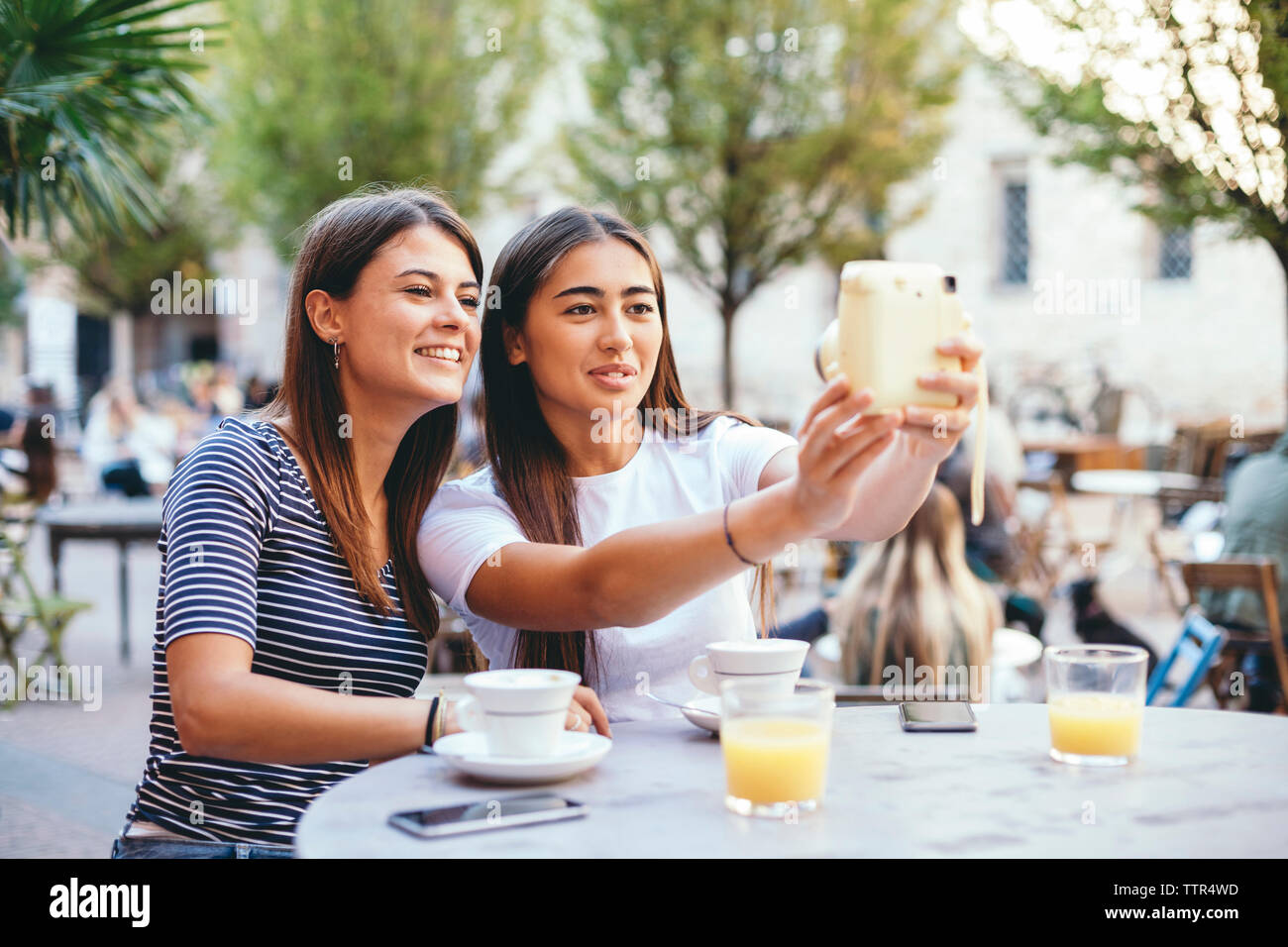 Weibliche Freunde unter selfie mit Instant Kamera beim Sitzen im Straßencafé Stockfoto