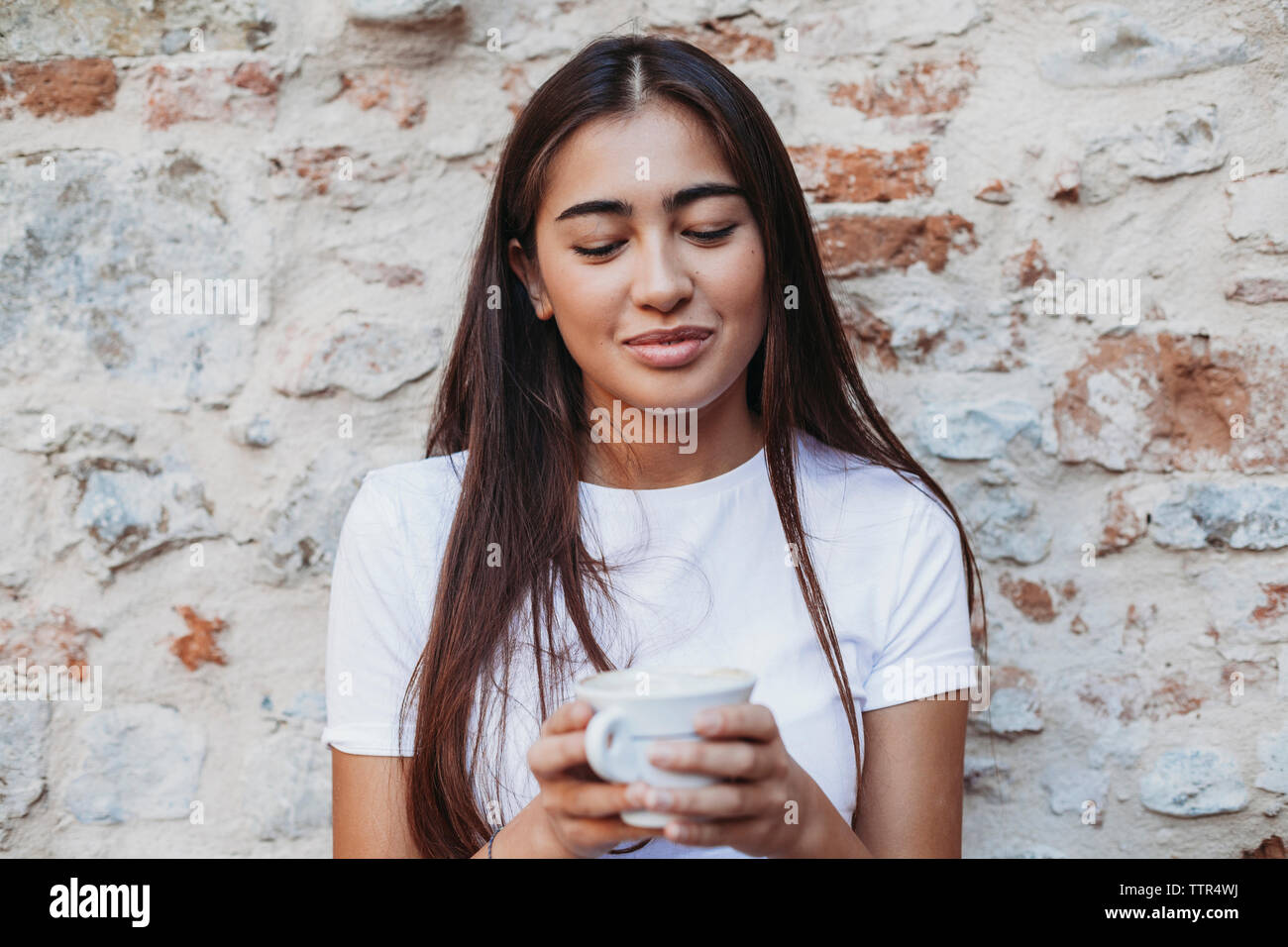 Frau mit Cappuccino, während sie von alten Ziegel Wand Stockfoto