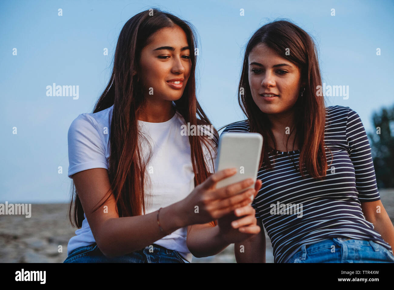 Weibliche Freunde auf der Suche nach smart phone gegen Himmel in Stadt Stockfoto