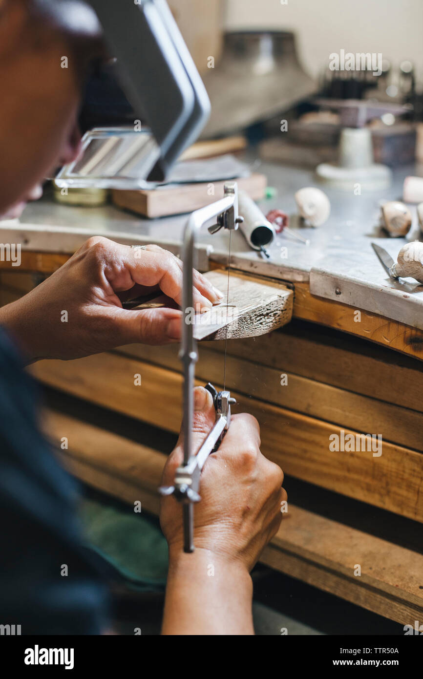 Zugeschnittenes Bild der weiblichen Handwerker mit handsäge während Herstellung von Schmuck auf hölzernen Tisch in Werkstatt Stockfoto