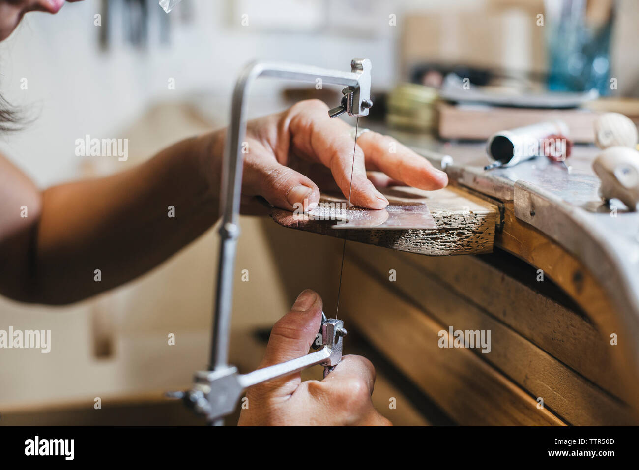 7/8 Hände der weiblichen Handwerker mit handsäge während Herstellung von Schmuck auf hölzernen Tisch in Werkstatt Stockfoto