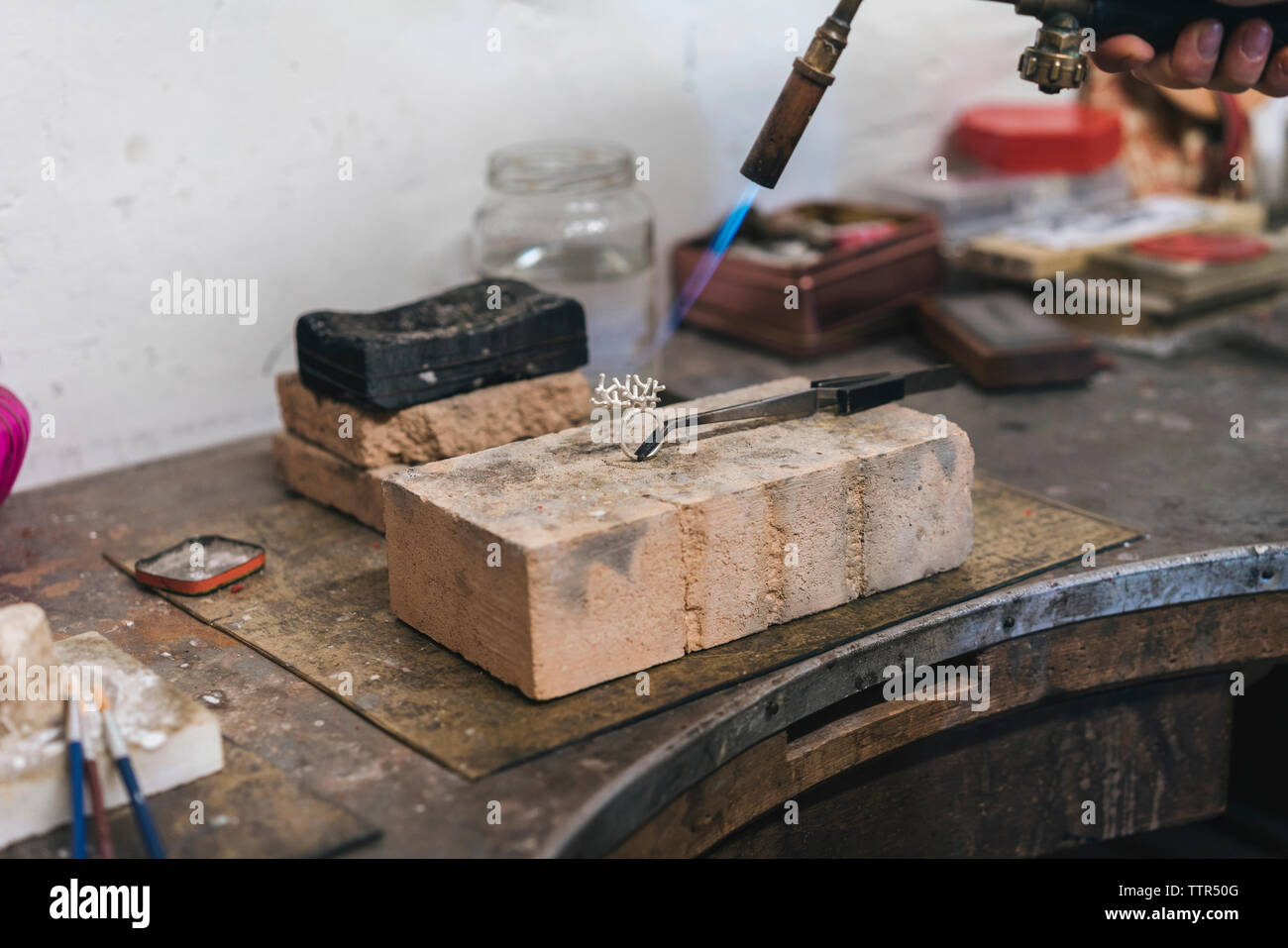 7/8-Seite der weiblichen Handwerker mit Brenner auf den Ring in der Werkstatt Stockfoto
