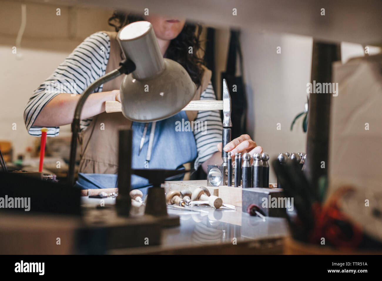 Mittelteil der weiblichen Handwerker mit Handwerkzeugen während Herstellung von Schmuck am Tisch in der Werkstatt Stockfoto
