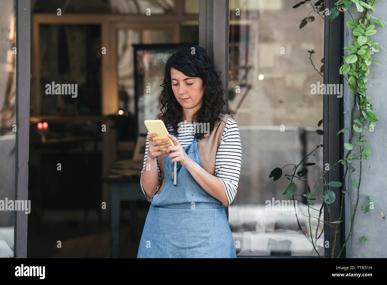 Zuversichtlich, dass weibliche Handwerker mit Smart Phone beim Stehen an der Tür in der Werkstatt Stockfoto