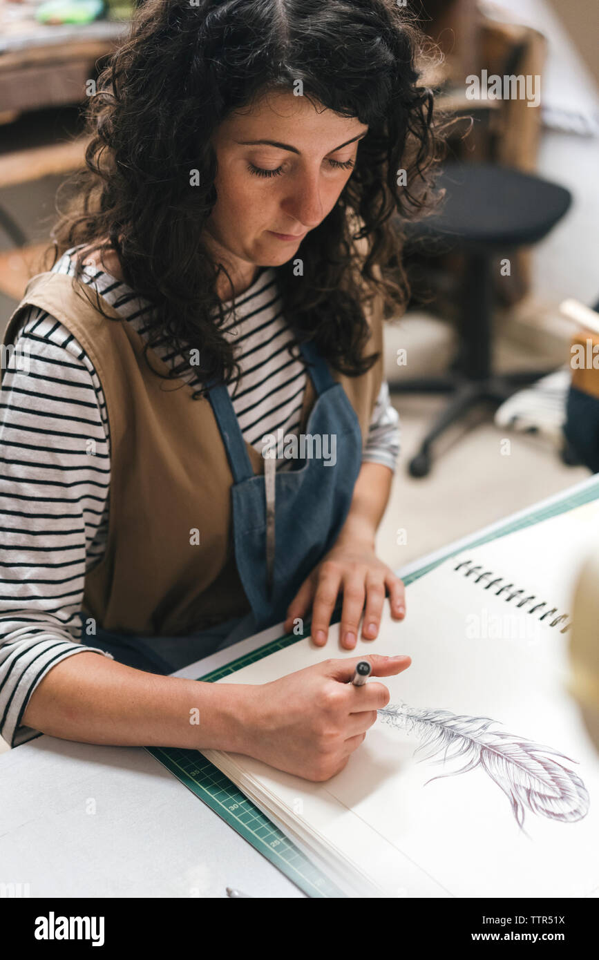 Hohe Betrachtungswinkel der weiblichen artisan Zeichnung auf Buch während der Sitzung in Werkstatt Stockfoto