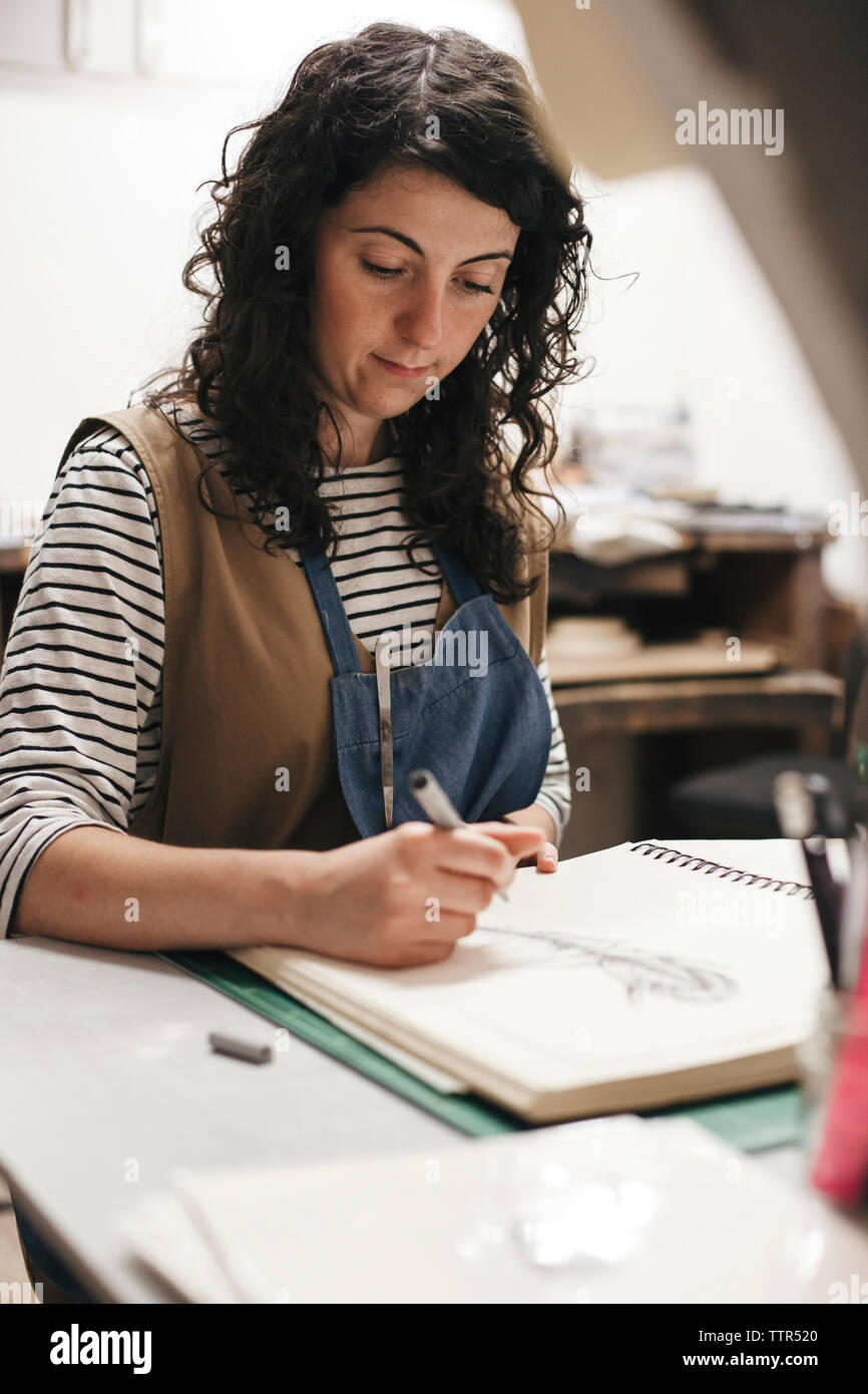 Weibliche Handwerker Zeichnung auf Buch während der Sitzung in Werkstatt Stockfoto