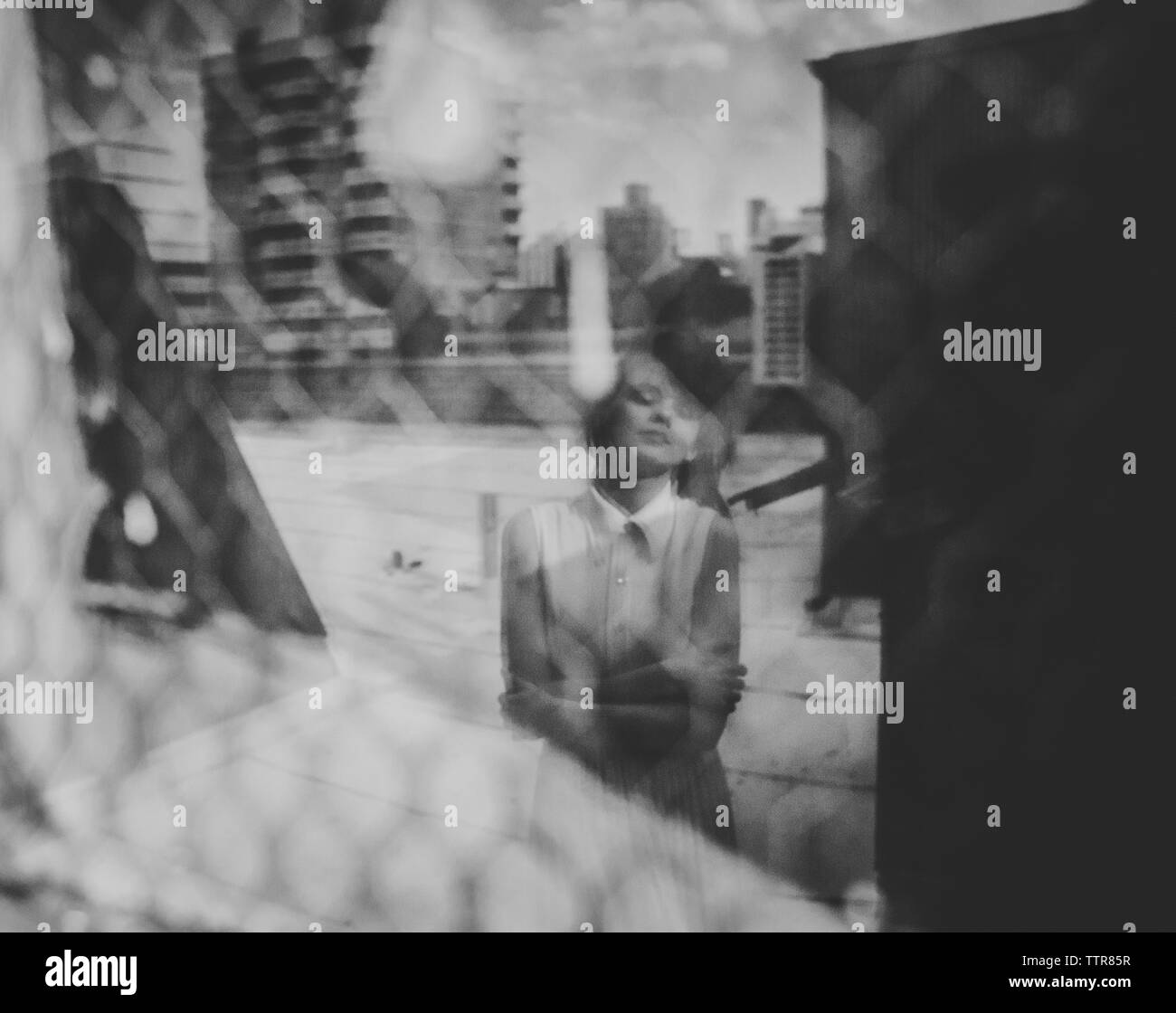 Frau mit verschränkten Armen auf Glas im Stehen an Gebäude Terrasse widerspiegelt Stockfoto