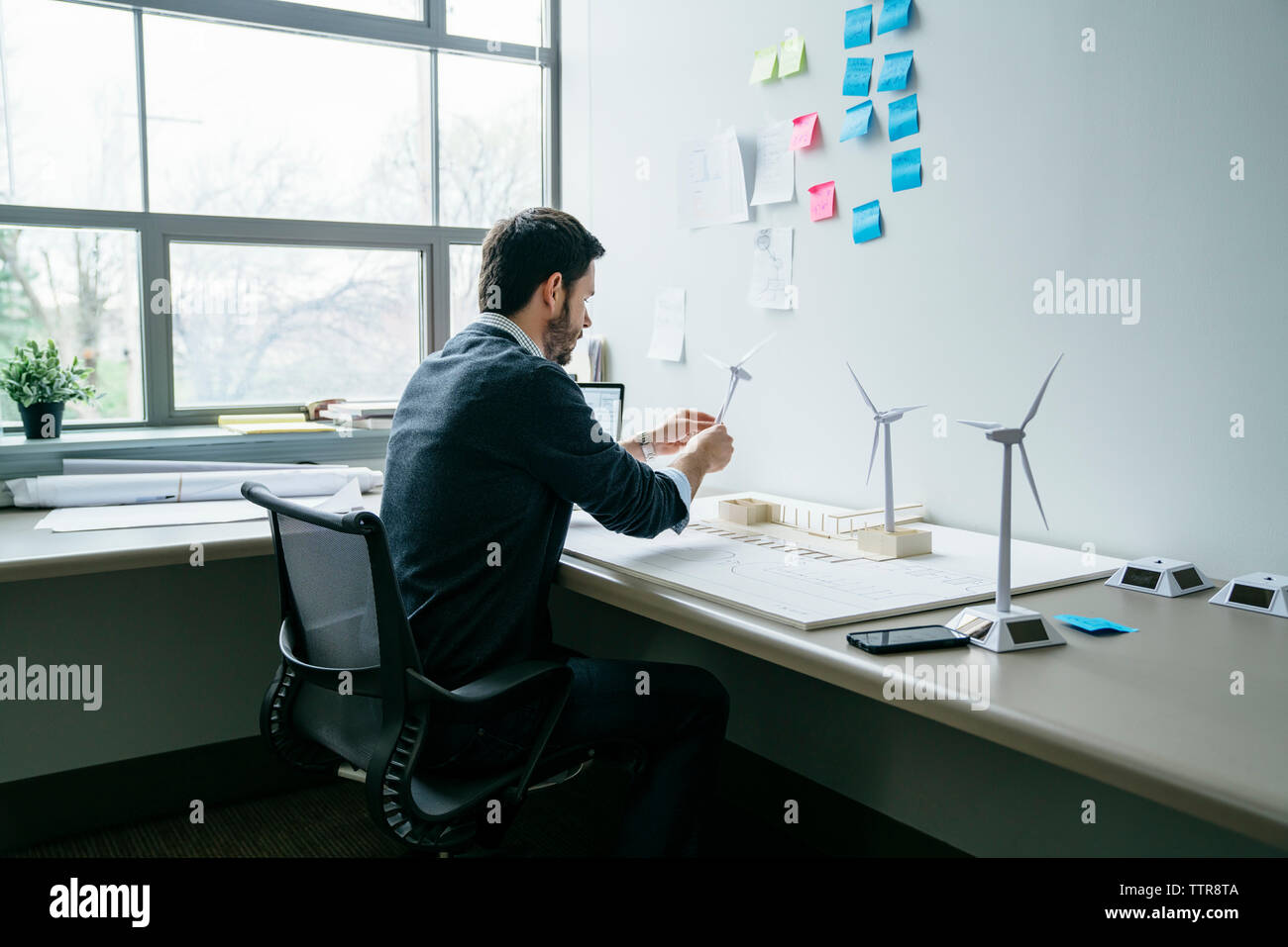 Geschäftsmann arrangiert Windkraftanlagenmodelle auf dem Schreibtisch Stockfoto