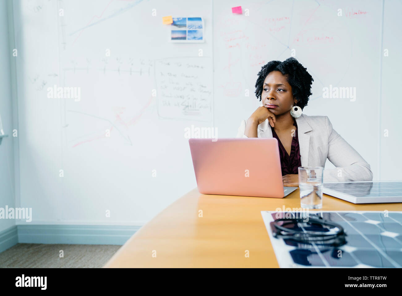 Nachdenklich Geschäftsfrau mit Hand am Kinn sitzen gegen Whiteboard im Büro Stockfoto