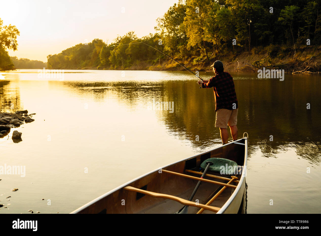 Ansicht der Rückseite des Mitte der erwachsene Mann angeln im Stehen mit dem Boot in See bei Sonnenuntergang Stockfoto