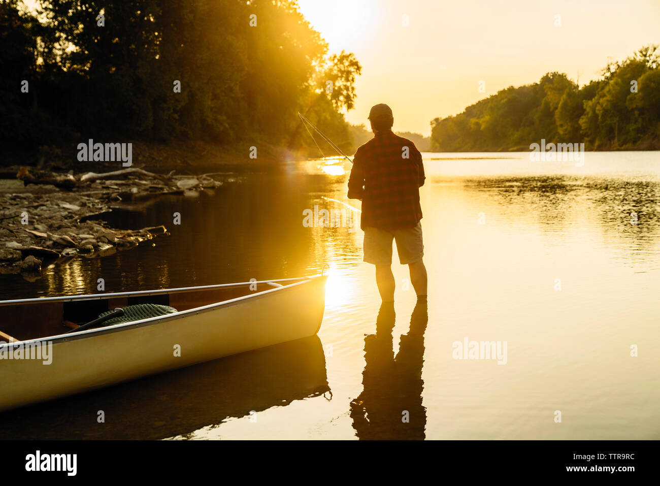 Ansicht der Rückseite des Mitte der erwachsene Mann angeln beim Stehen in der See bei Sonnenuntergang Stockfoto