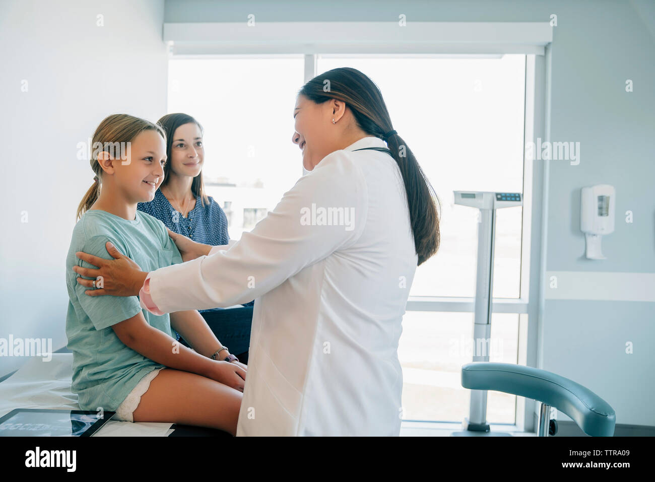 Fröhlich Kinderarzt sprechen mit Patienten sitzend durch Mutter im Untersuchungsraum Stockfoto