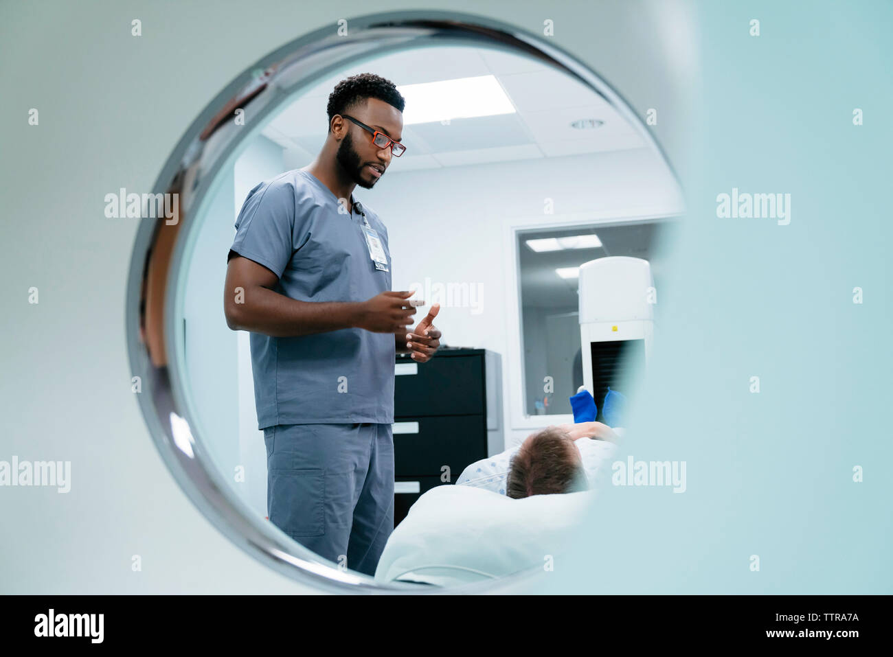 Männliche Krankenschwester im Gespräch mit Patient im Untersuchungsraum durch MRT-Scanner gesehen Stockfoto