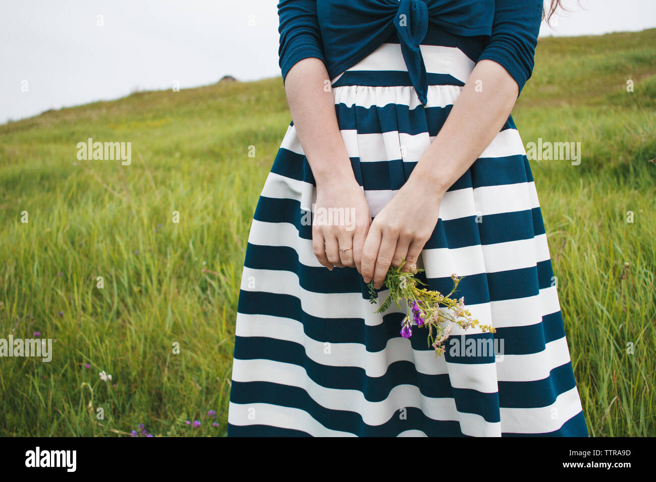 Mittelteil der Frau mit Blumen und auf der Wiese Stockfoto