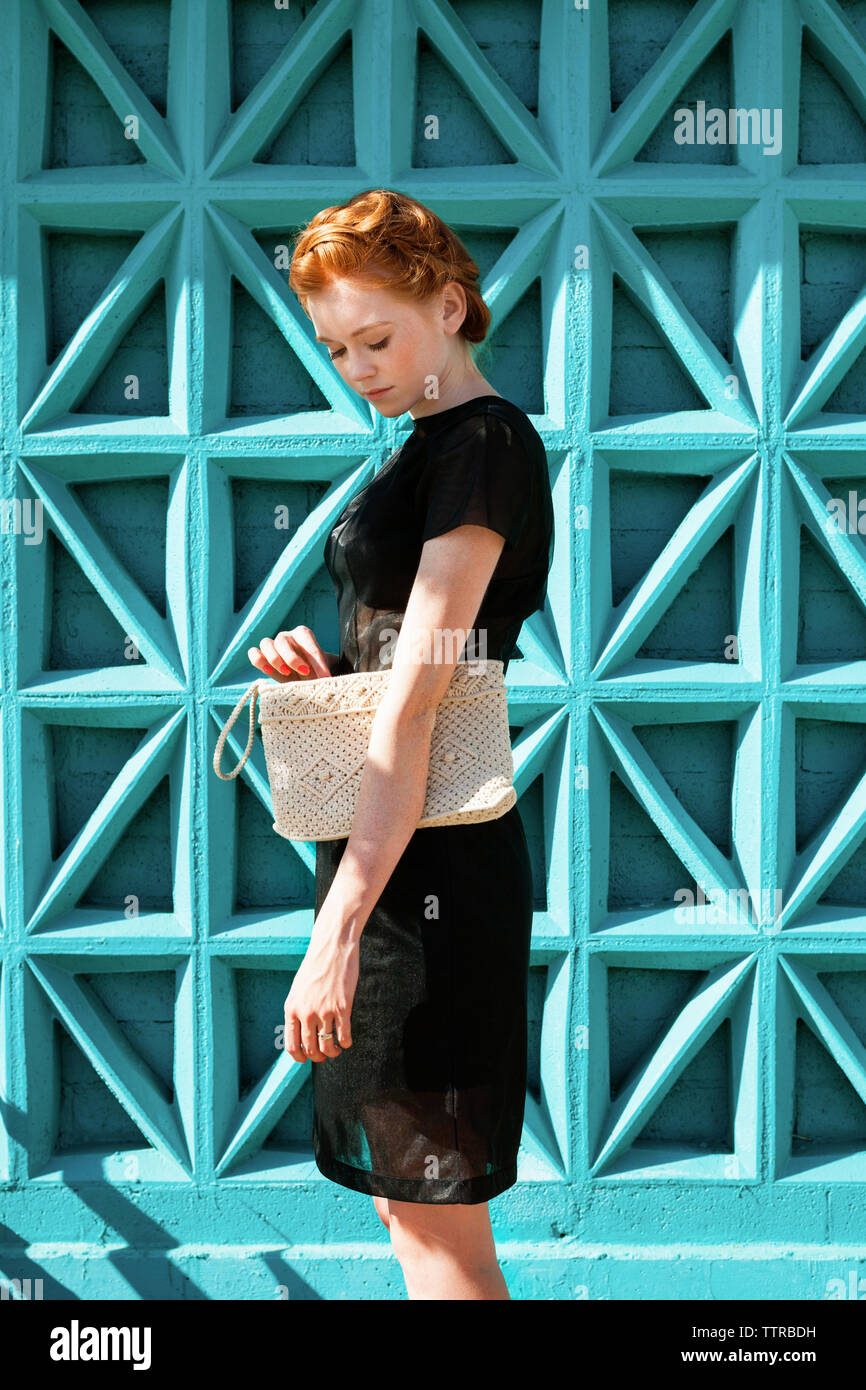 Seitenansicht der jungen Frau, die Clutch Bag gegen blaue Wand Stockfoto