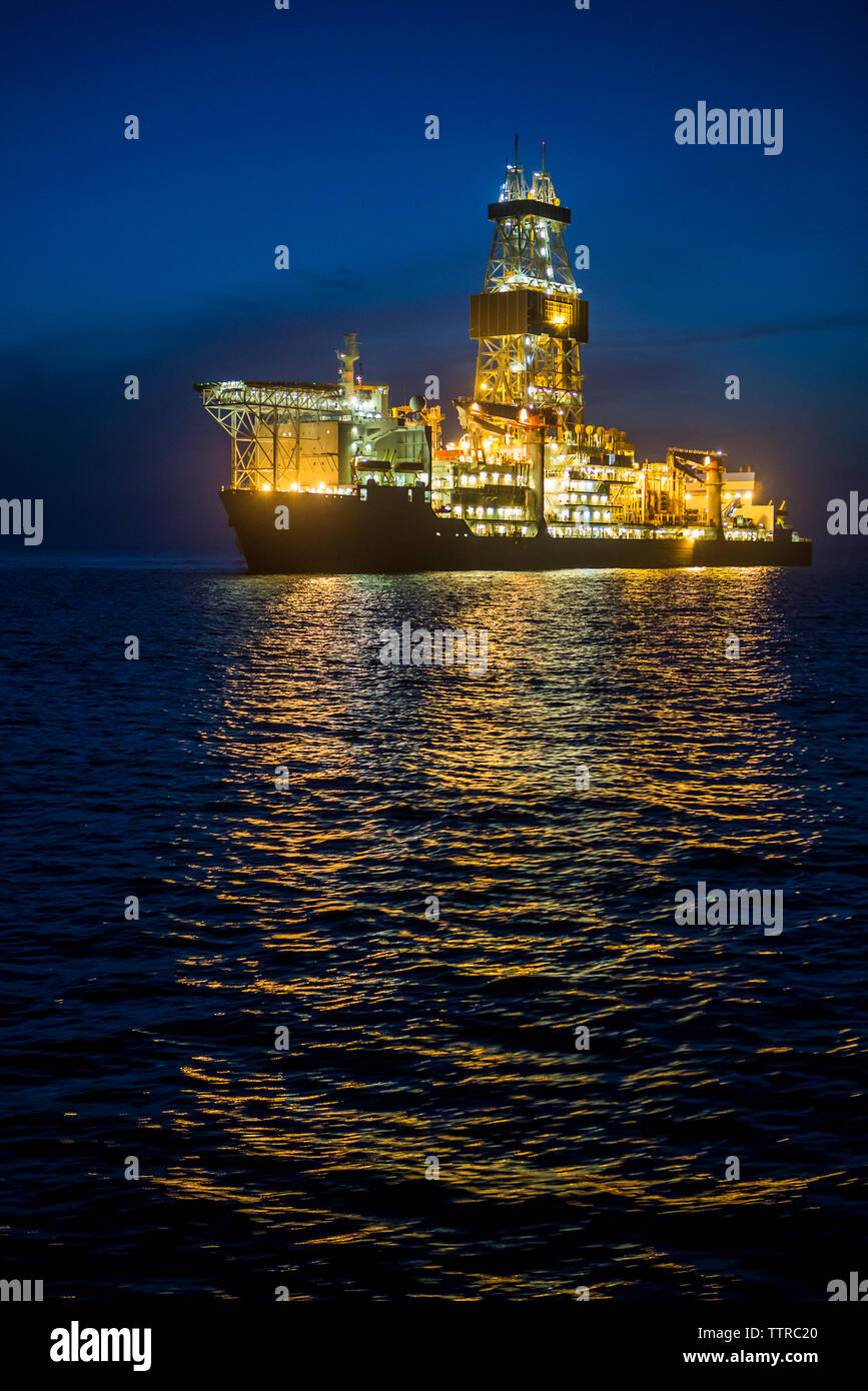 Beleuchtete bohren Schiff auf dem Meer vor blauem Himmel bei Nacht Stockfoto
