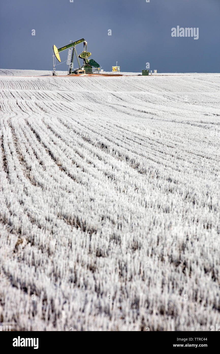 Mitte der Abstand von pumpjack am Ölindustrie über Feld gegen Himmel im Winter Stockfoto