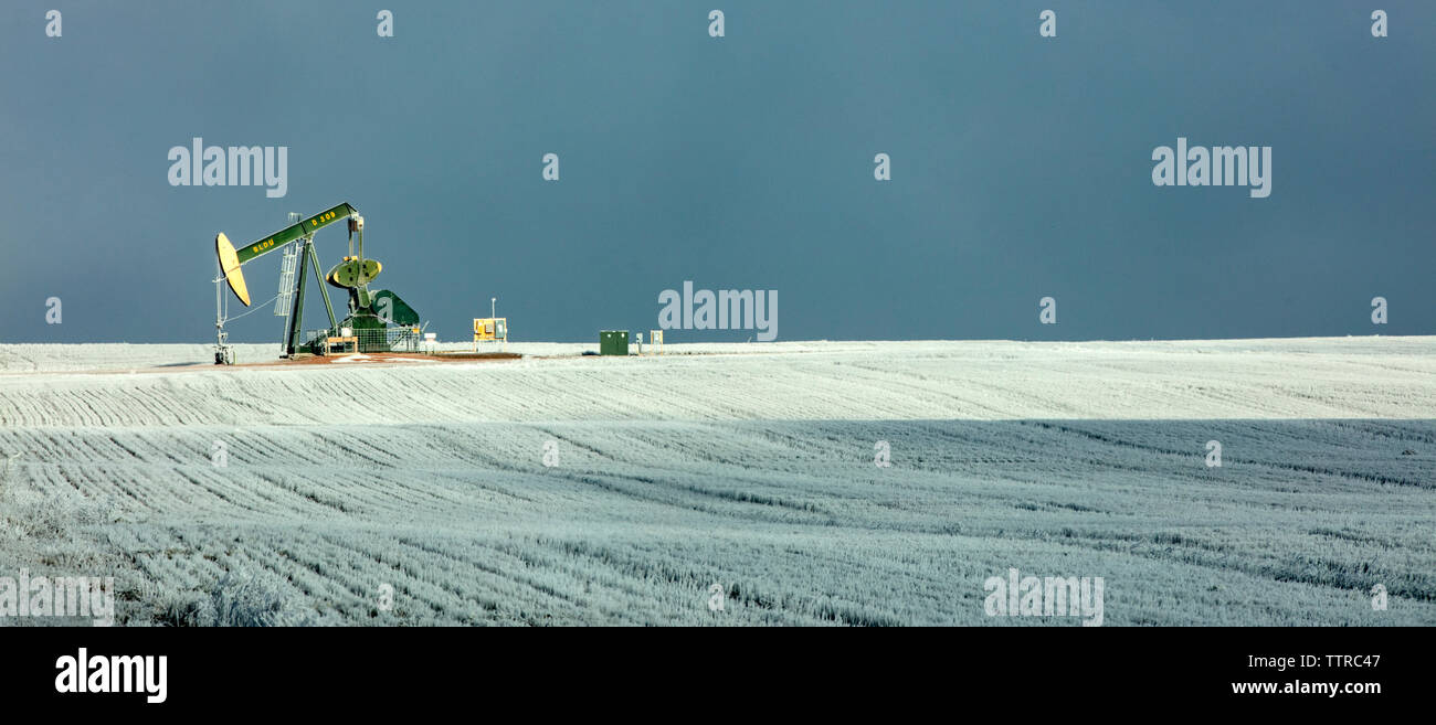 Panoramablick auf pumpjack am Ölindustrie über Feld gegen Himmel im Winter Stockfoto