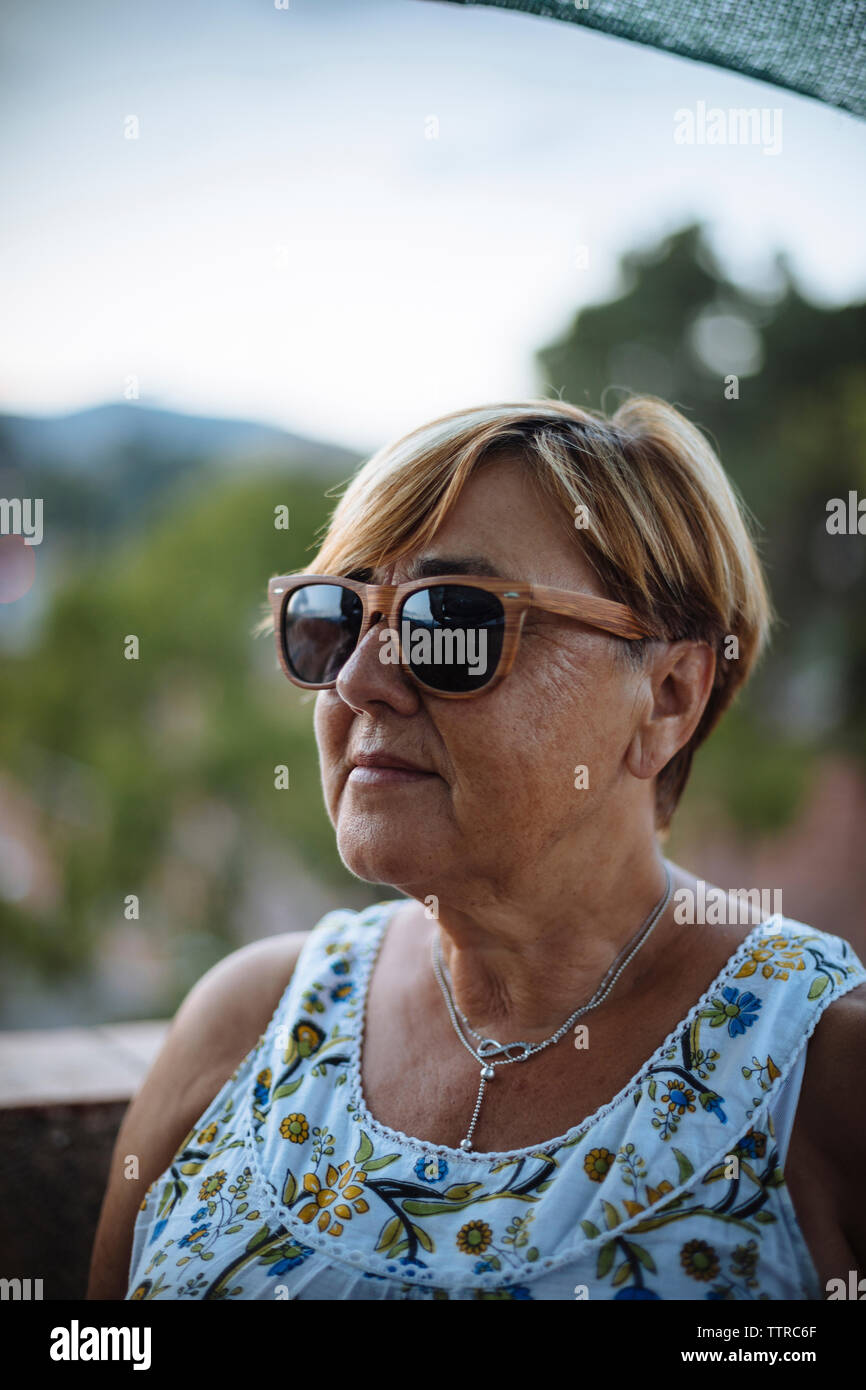 Nahaufnahme der älteren Frau mit Sonnenbrille beim Stehen auf Gebäude Terrasse gegen Sky Stockfoto