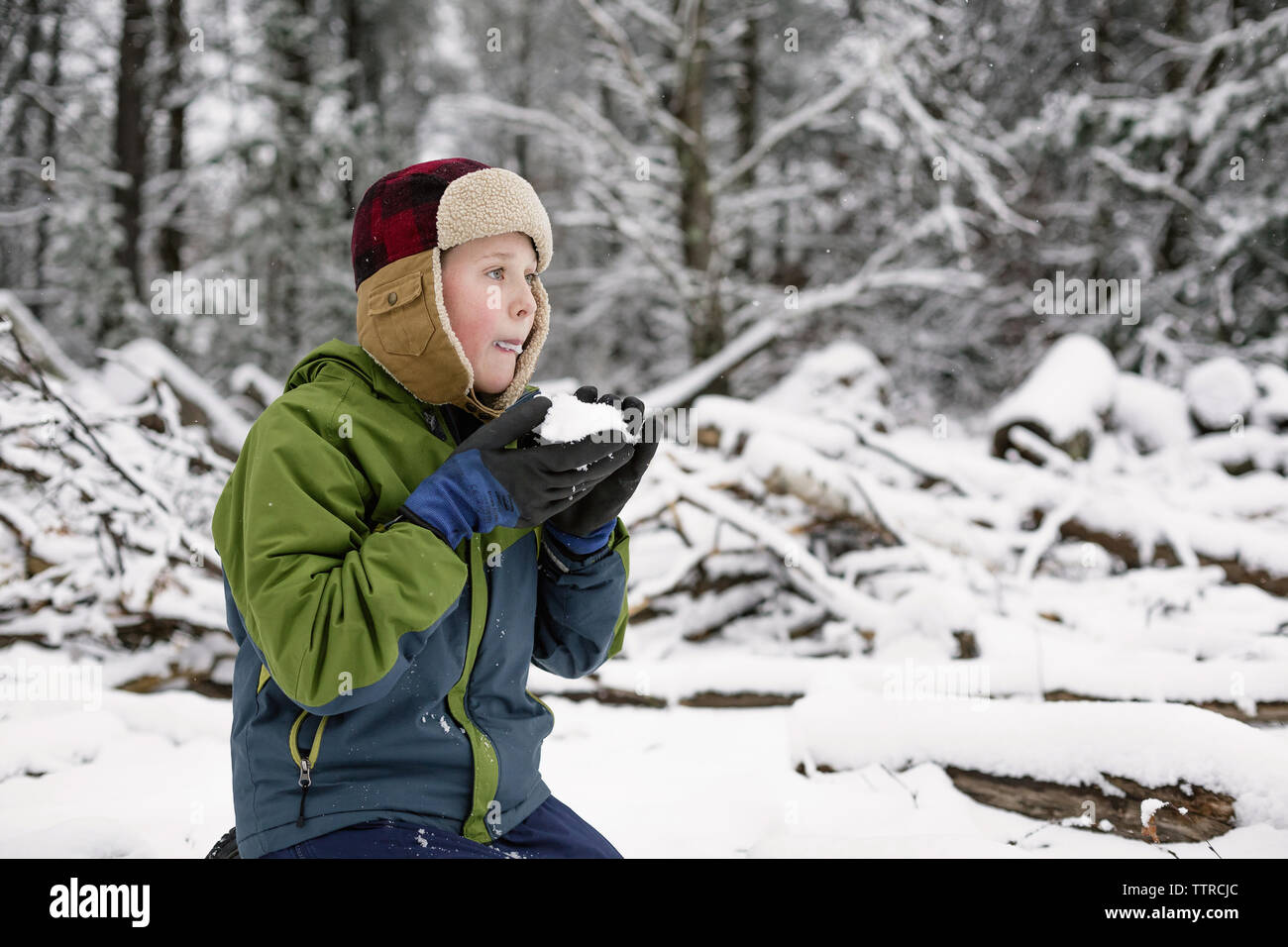 Junge essen Schnee während kniend auf Feld Stockfoto