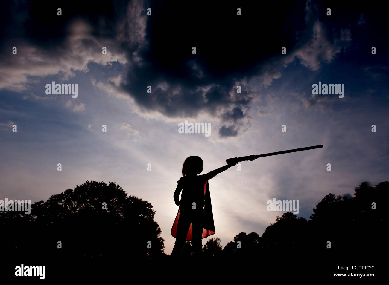 Low Angle View von Silhouette Mädchen in Tracht holding Schwert beim Stehen gegen Himmel im Park bei Sonnenuntergang Stockfoto