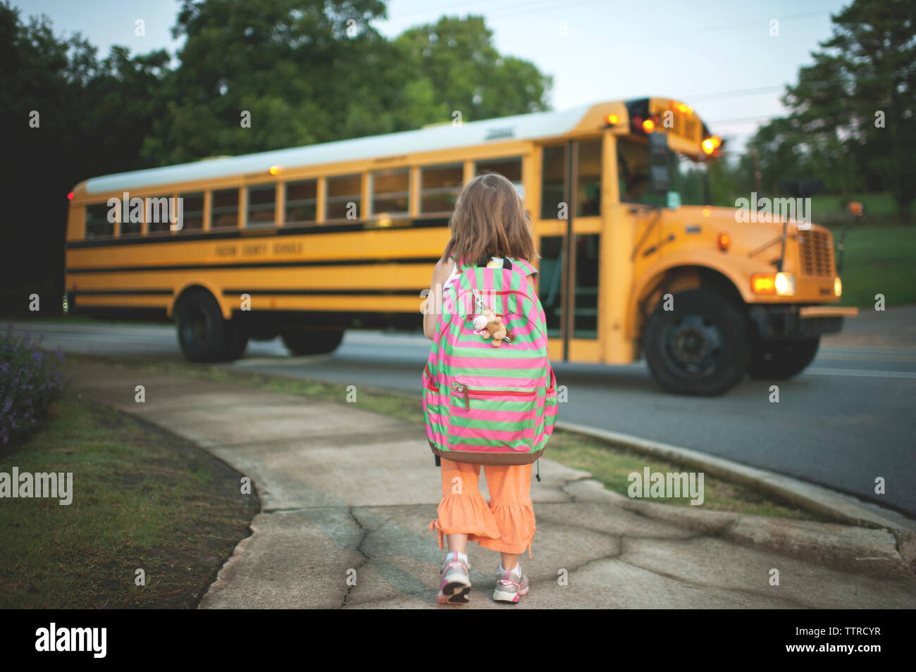 Ansicht der Rückseite des Schulmädchen mit Rucksack Warten auf dem Bus beim Stehen auf Fußweg Stockfoto