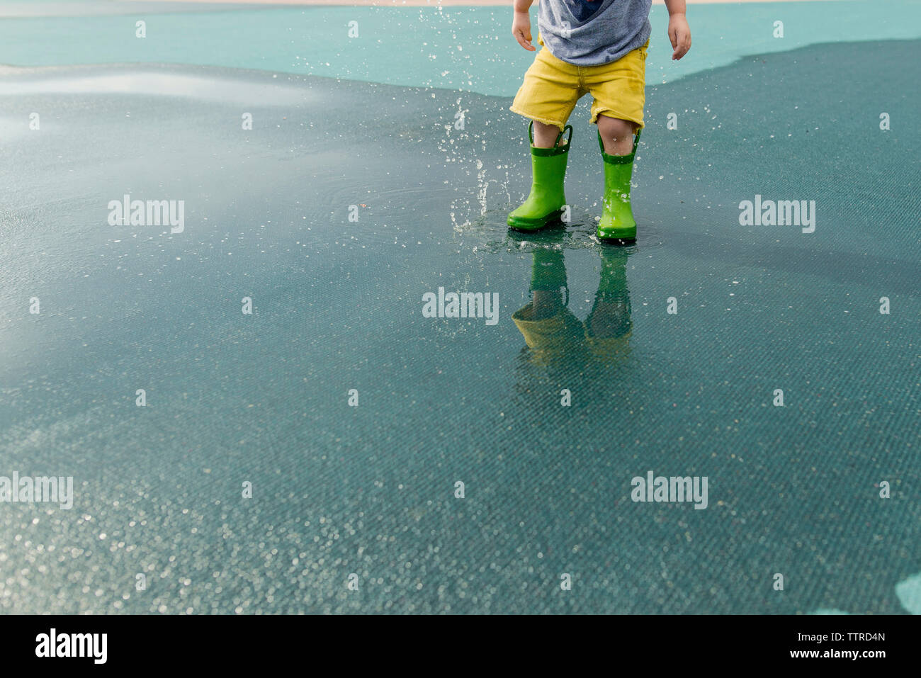 Untere Partie des Jungen in Gummistiefel Spritzwasser auf nassen Straßen Stockfoto
