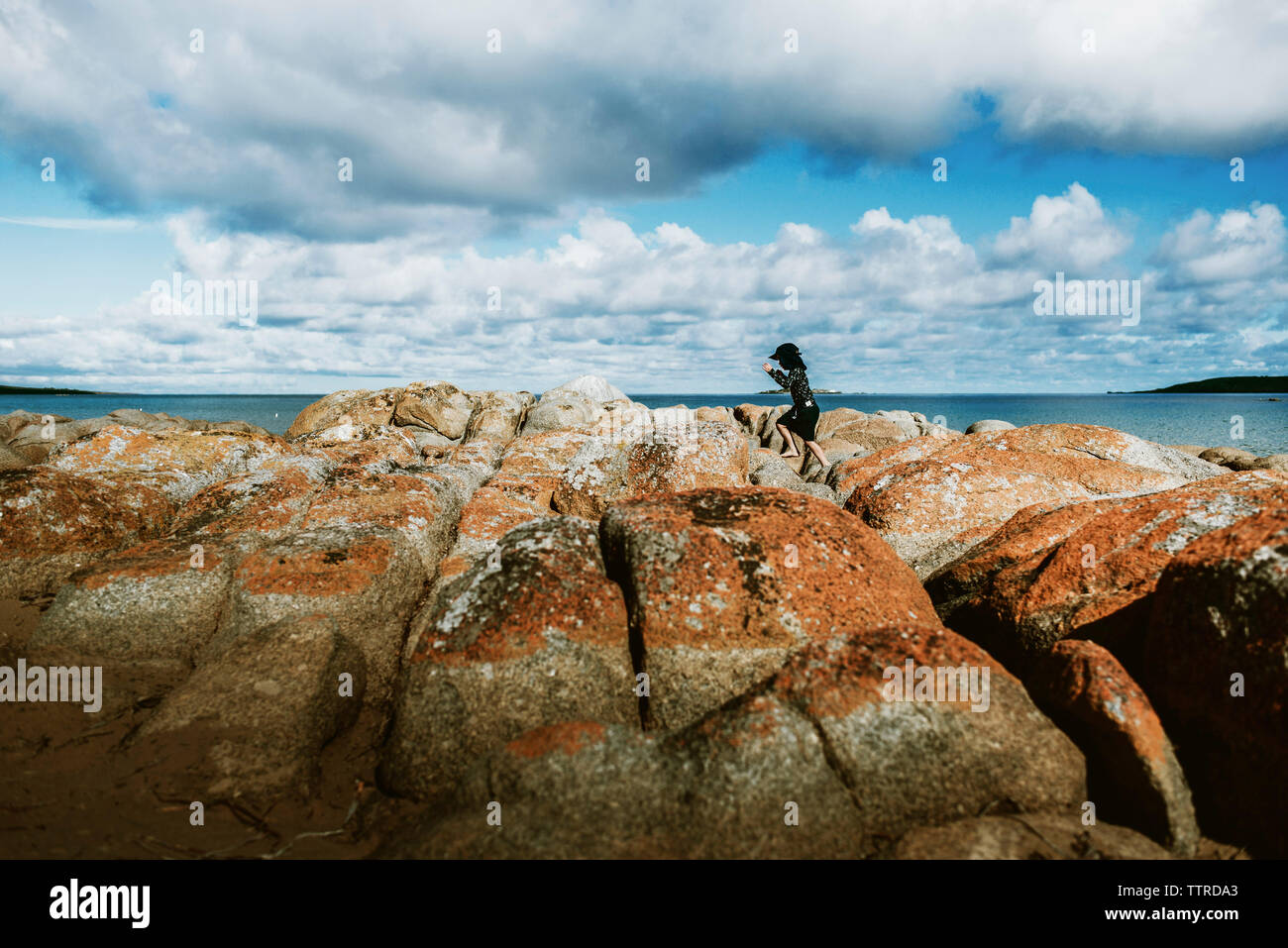 Seitenansicht der Frau springen auf Felsen am Strand gegen bewölkter Himmel Stockfoto