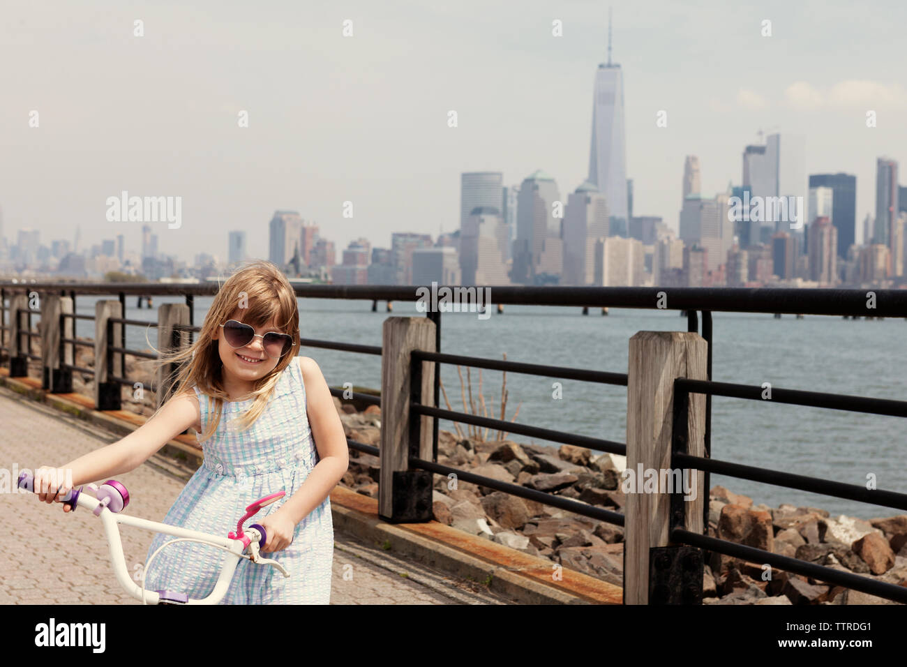 Portrait von Mädchen mit dem Fahrrad auf der Promenade mit Sicht auf die City Skyline im Hintergrund Stockfoto