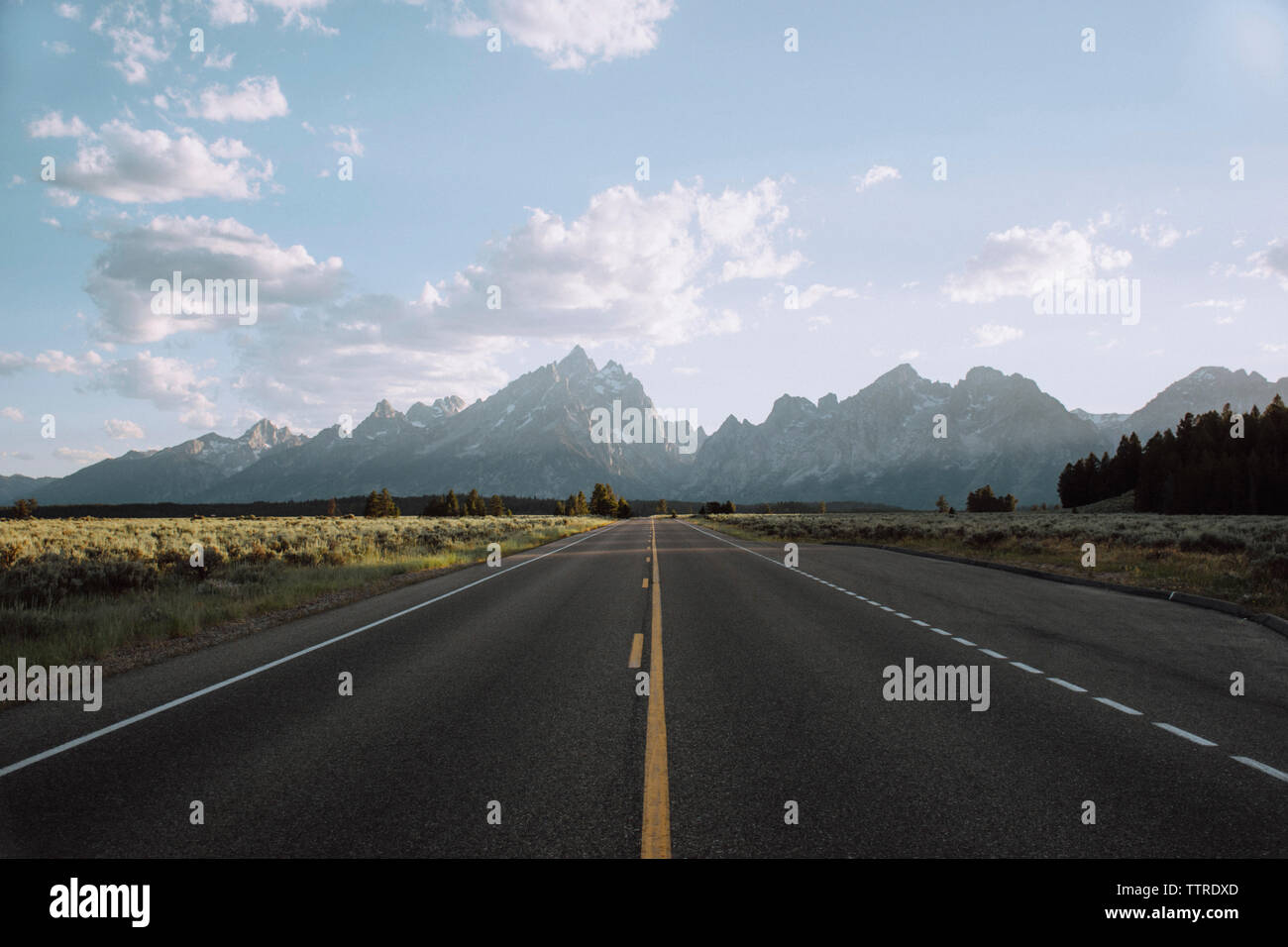 Leere Landstraße inmitten von Feld in Richtung Berge gegen Himmel führenden Stockfoto