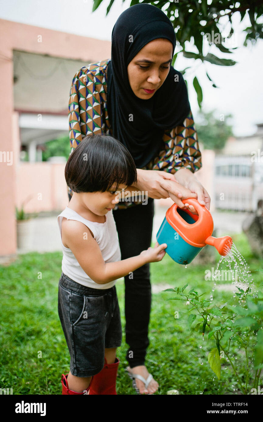 Mutter mit Sohn Bewässerung von Pflanzen im Hinterhof Stockfoto