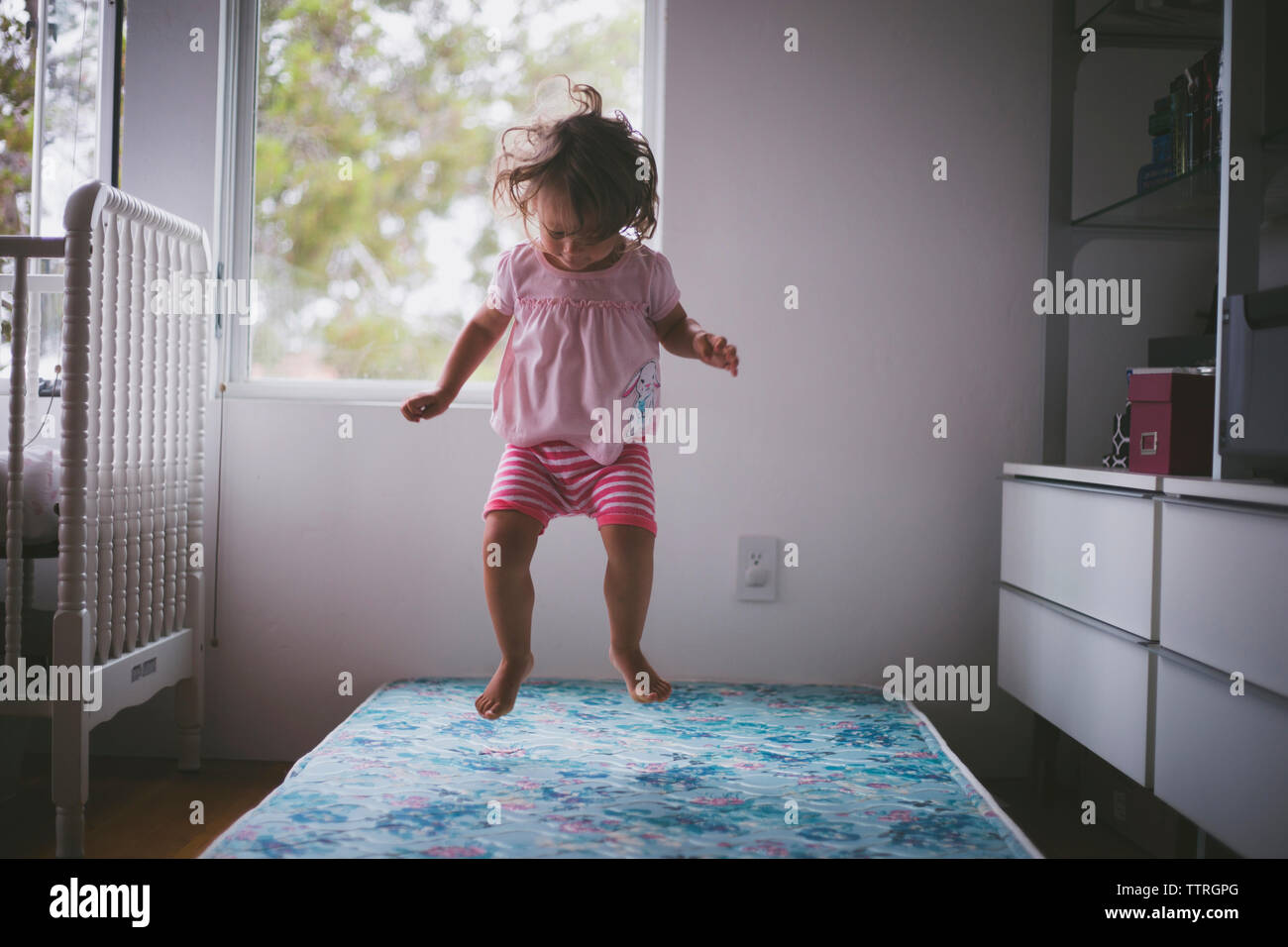 Fröhliches Mädchen springen auf Bett zu Hause Stockfoto