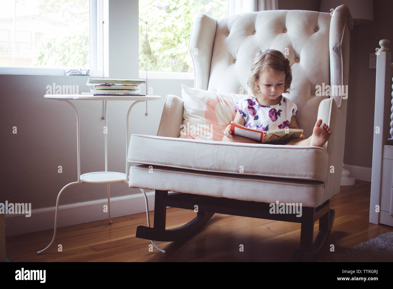 Mädchen lesen Bild Buch während auf Schaukelstuhl zu Hause sitzen Stockfoto