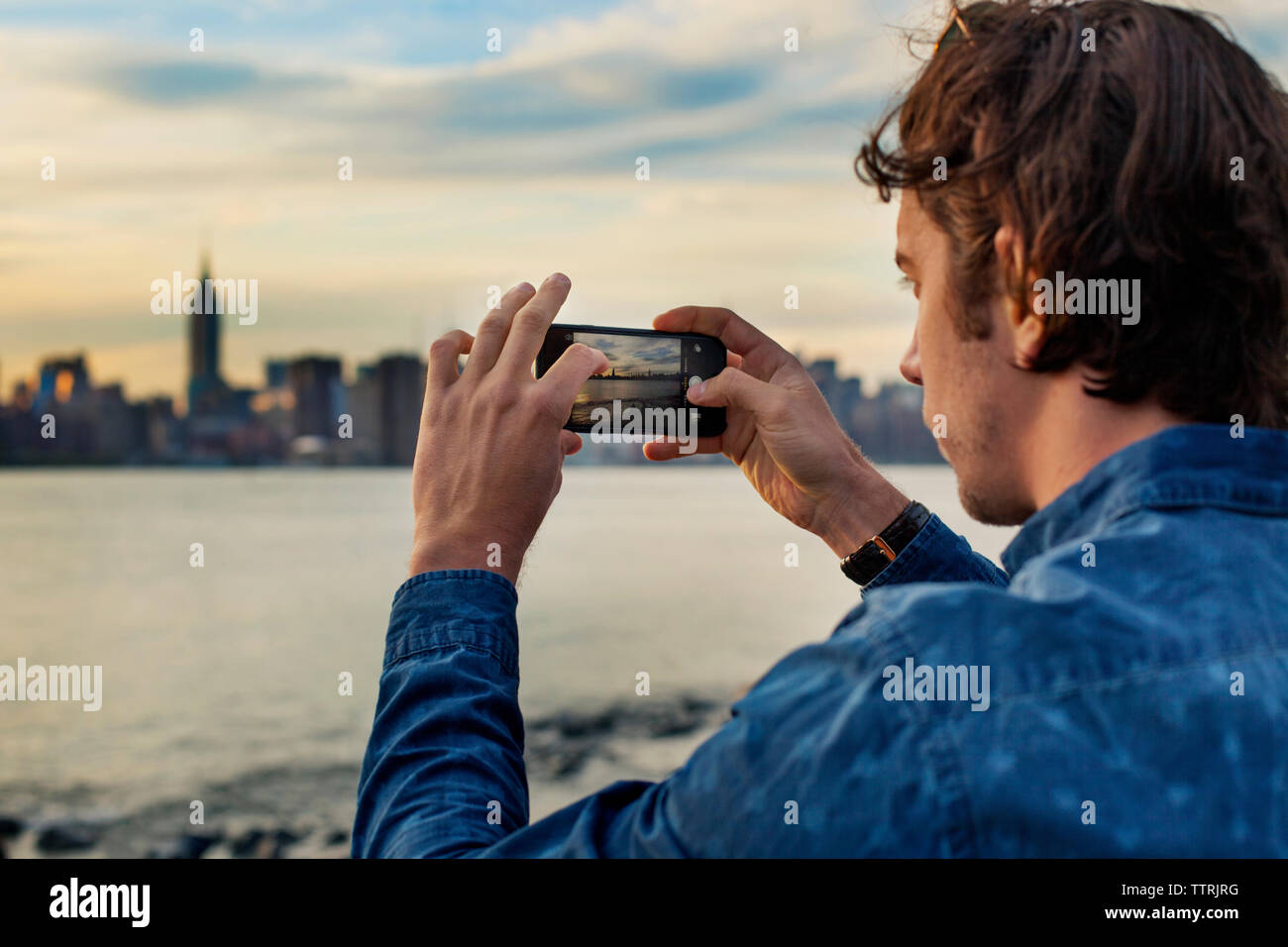 Mann fotografieren Stadt und Meer mit smart phone bei Sonnenuntergang Stockfoto