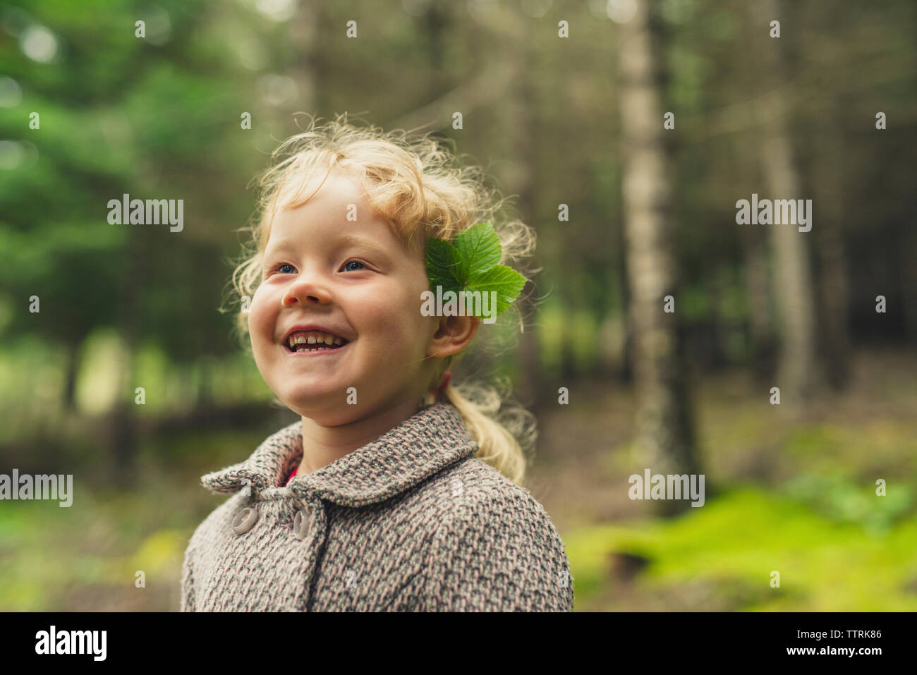 Fröhliches Mädchen mit Blättern am Ohr am Wald Stockfoto