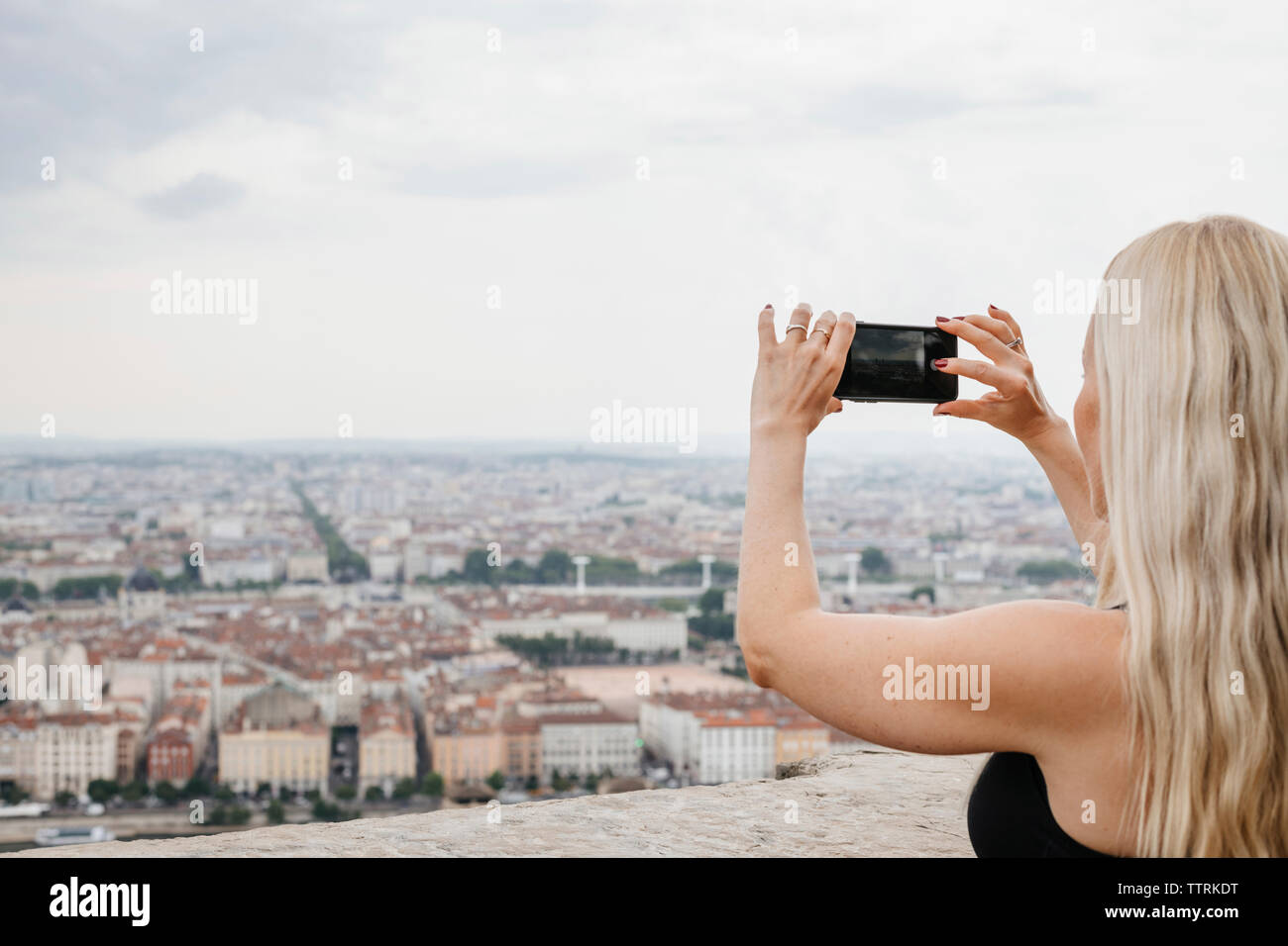 Seitenansicht der Frau fotografieren Stadtbild mit Smart Phone beim Stehen gegen Sky Stockfoto