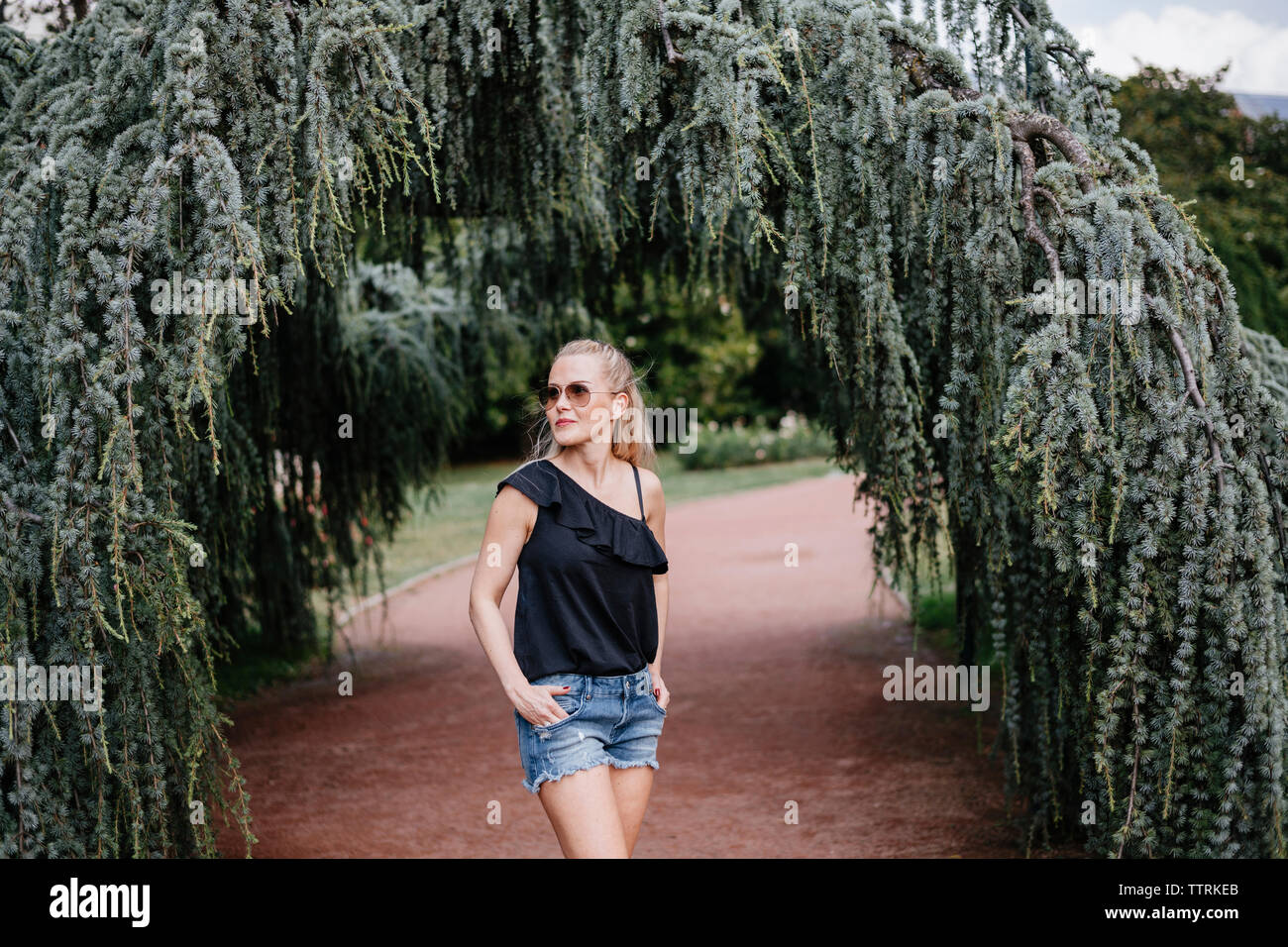 Stilvolle Frau mit Händen in den Taschen Sonnenbrillen tragen, während auf Wanderweg in PARK-Stellung Stockfoto