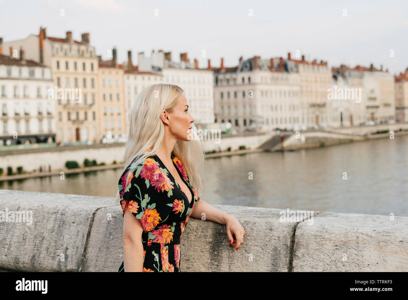 Seitenansicht der nachdenkliche Frau, die auf eine Fußgängerbrücke über den Fluss gegen Gebäude in der Stadt Stockfoto