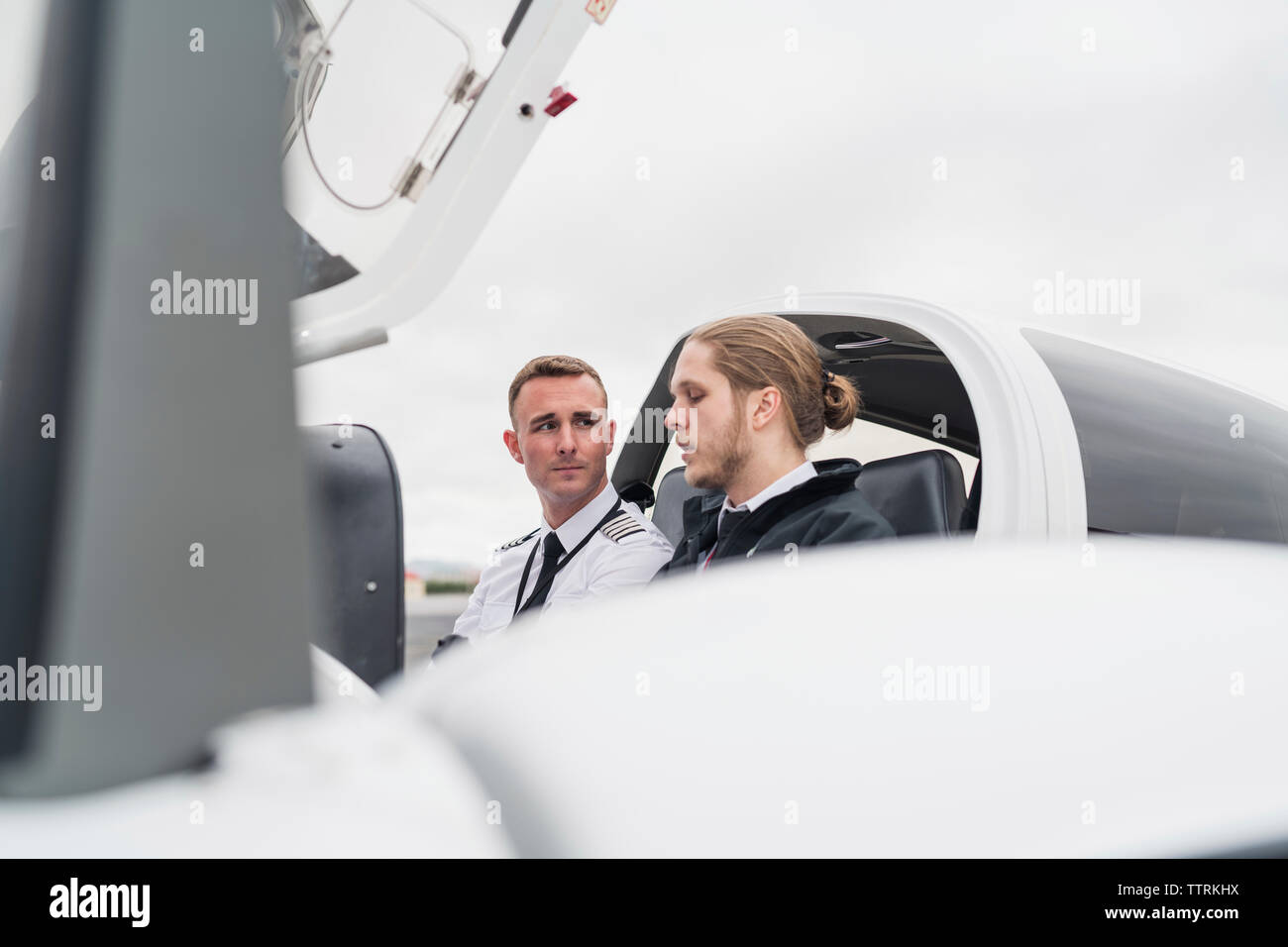Männliche Piloten sprechen während der Sitzung in Flugzeug gegen bewölkter Himmel Stockfoto
