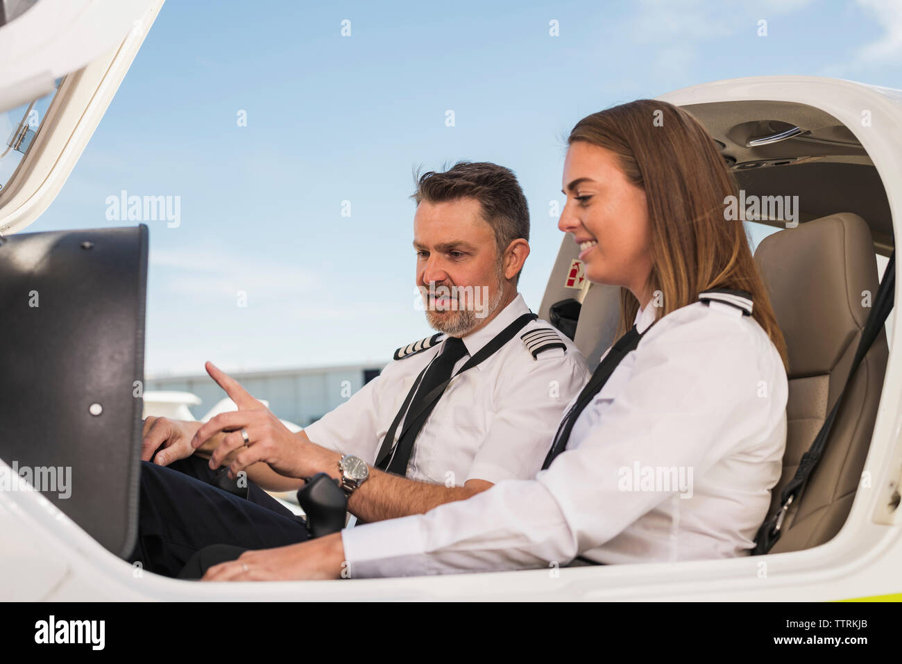 Männliche pilot Lehre weiblicher Auszubildender in Flugzeug gegen den blauen Himmel am Flughafen Stockfoto