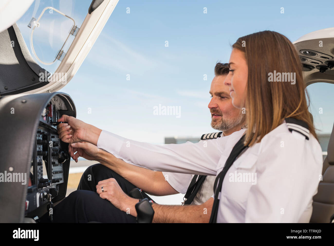 Seitenansicht der männlichen pilot Lehre weiblichen Auszubildenden Control Panel im Flugzeug gegen den blauen Himmel zu am Flughafen betreiben Stockfoto
