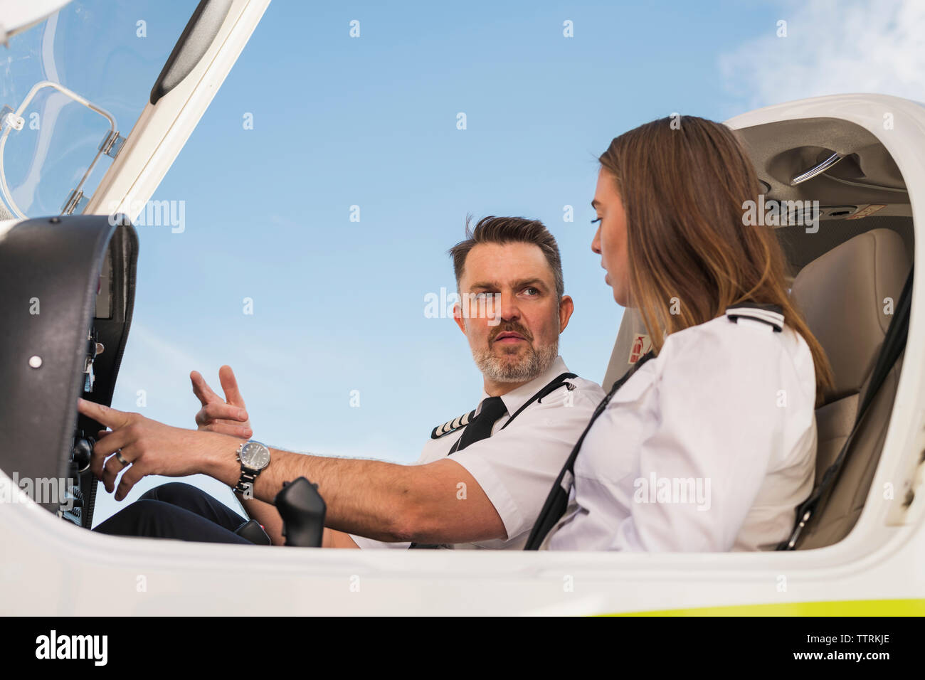 Low Angle View der männlichen pilot Lehre trainee Control Panel im Flugzeug gegen den blauen Himmel zu am Flughafen betreiben Stockfoto